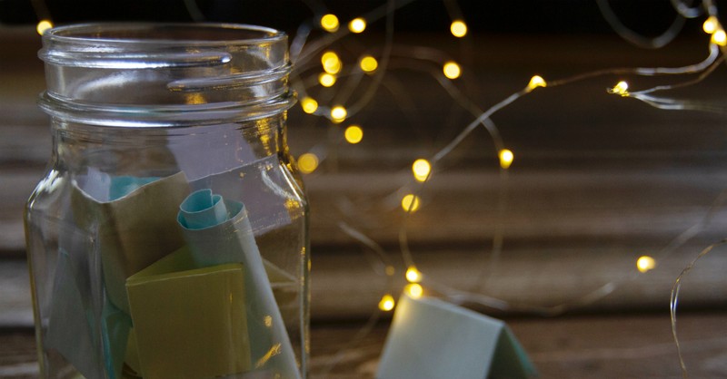 Glass jar filled with colorful notes, surrounded by soft fairy lights on a wooden surface.