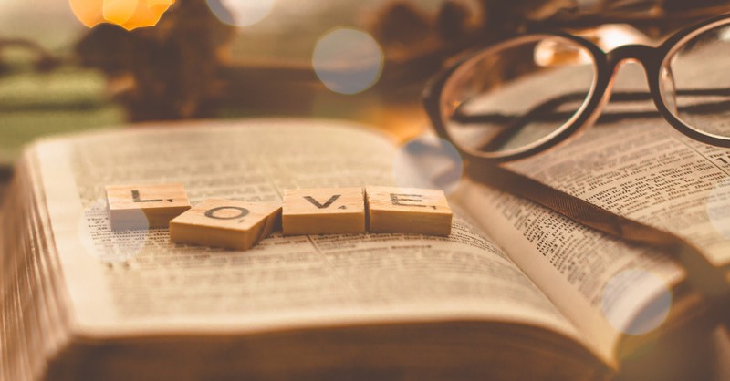 Open book with Scrabble tiles spelling "LOVE," alongside glasses, creating a warm, cozy atmosphere.