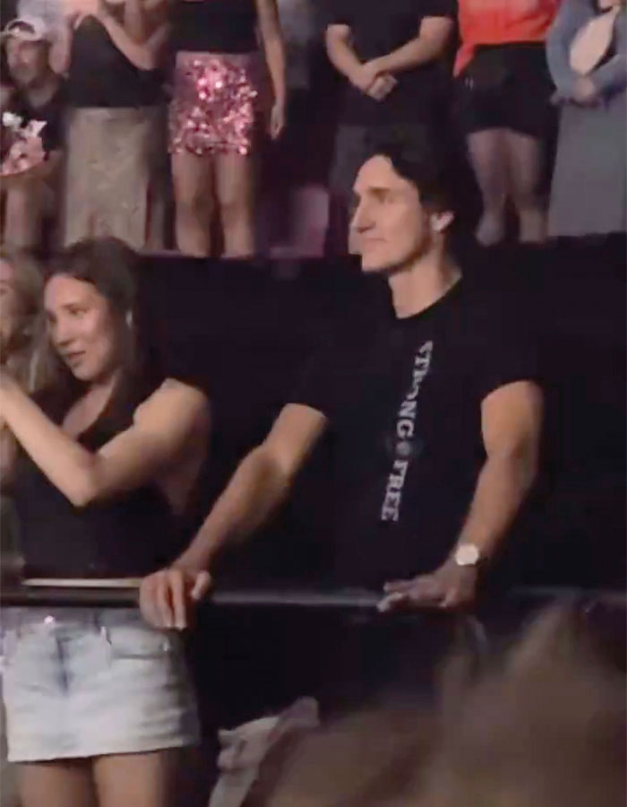 Man and woman enjoying a live concert, standing by a railing, surrounded by a crowd.