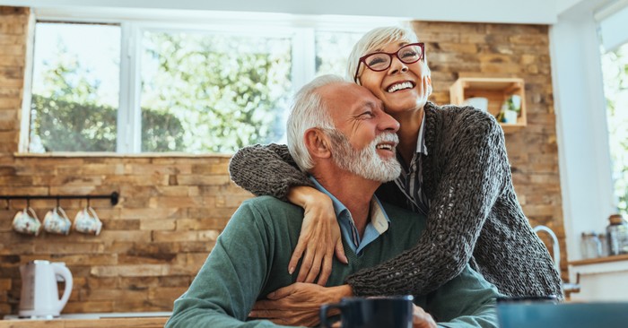 Elderly couple enjoying a joyful embrace at a cozy kitchen table.