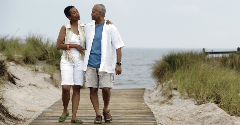 Elderly couple walking hand in hand on a beach boardwalk, smiling and enjoying a peaceful day by the ocean.