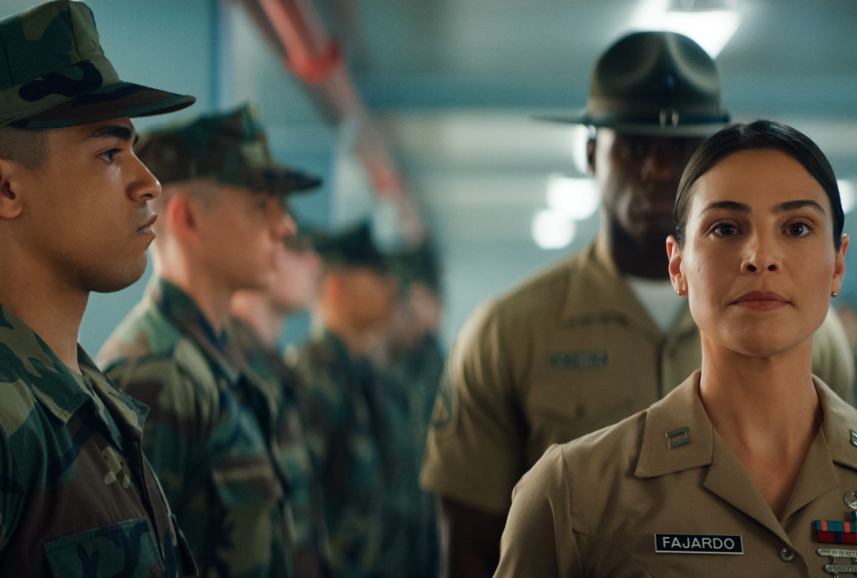 Military personnel in formation; a focused officer leads, with soldiers in uniform standing attentively in the background.