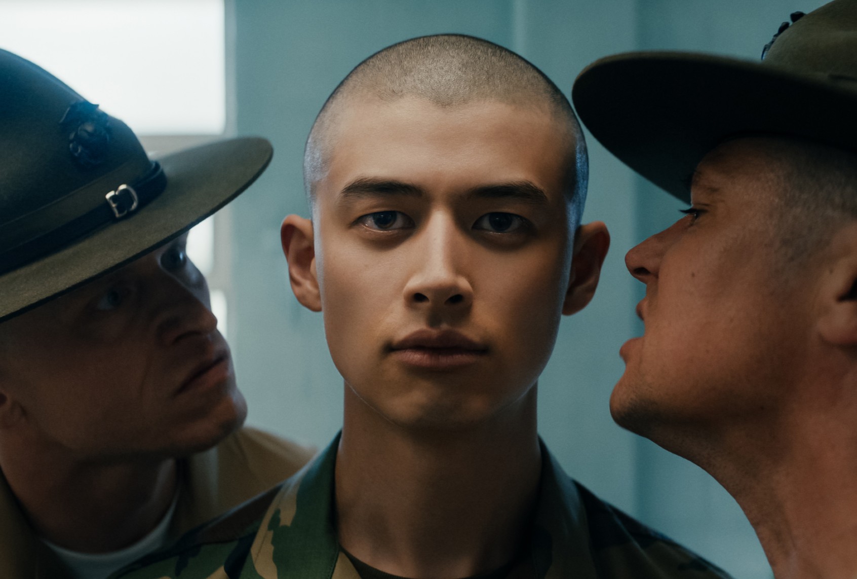 Drill sergeants shouting at a focused young soldier during training, with intense expressions and military uniforms.