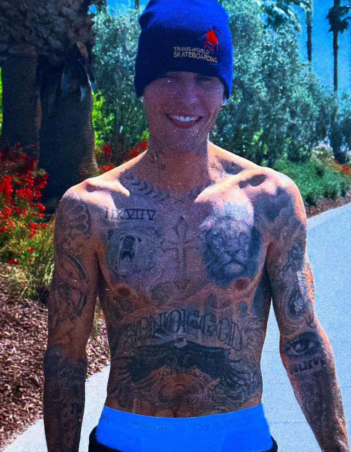 Shirtless man with extensive tattoos, wearing a beanie, smiling outdoors.
