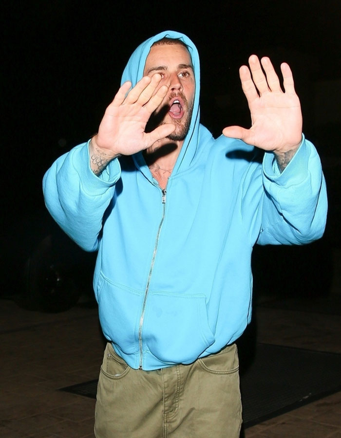 Person in a blue hoodie raising both hands to the camera, appearing surprised or defensive.