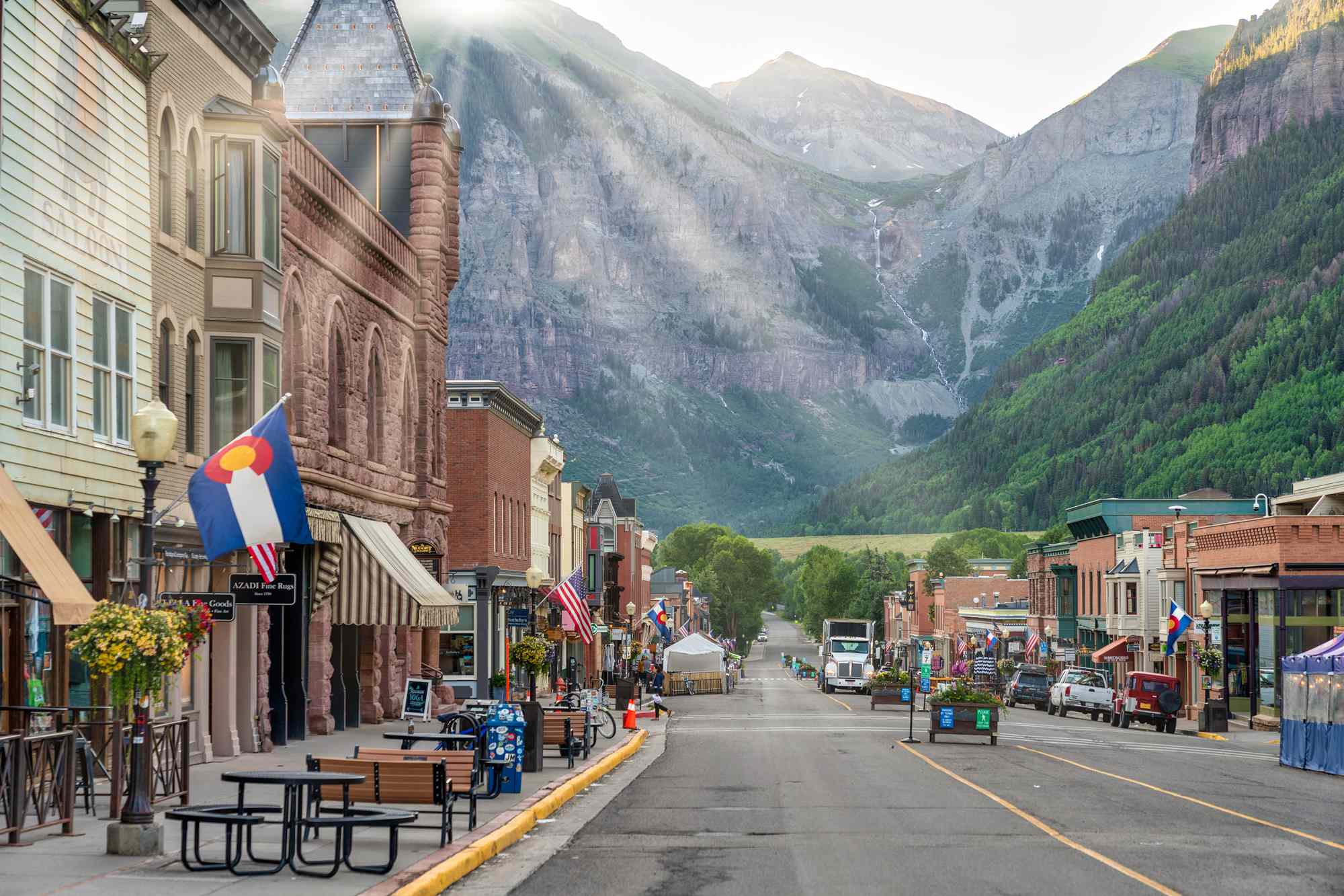 Charming mountain town street with colorful flags, historic buildings, and scenic backdrop under a bright, clear sky.