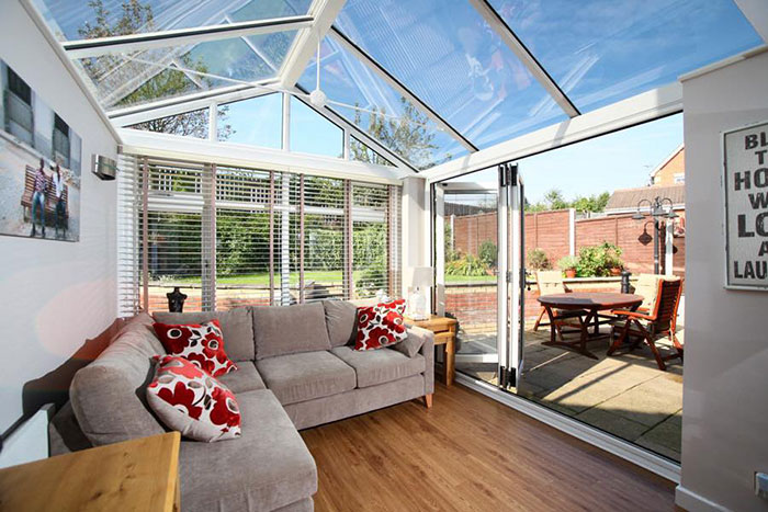 Bright and modern sunroom with glass ceiling and large open doors leading to an outdoor patio in a home setting.