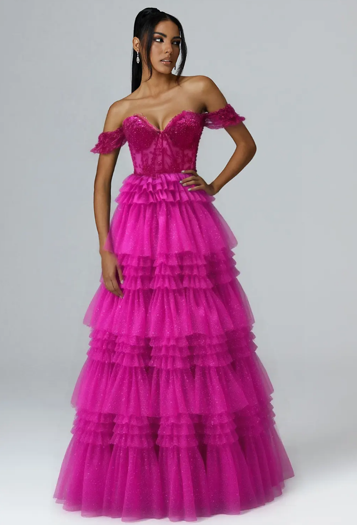 Woman in vibrant pink off-shoulder ruffled gown poses confidently against a plain background.