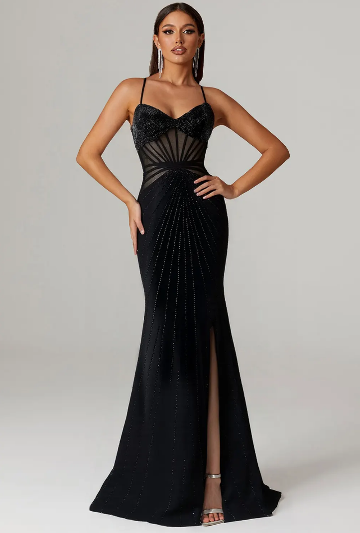Woman in elegant black evening gown with intricate detailing, posing confidently against a neutral background.