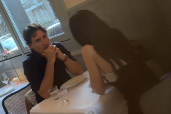Man and woman seated at a restaurant table, engaged in conversation with plates and glasses in front of them.