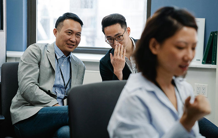 Two male co-workers whisper and make bets about a female colleague in a tense office environment.