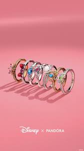 Collection of Disney x Pandora rings displayed on a pink background, featuring various colorful gemstones and designs.