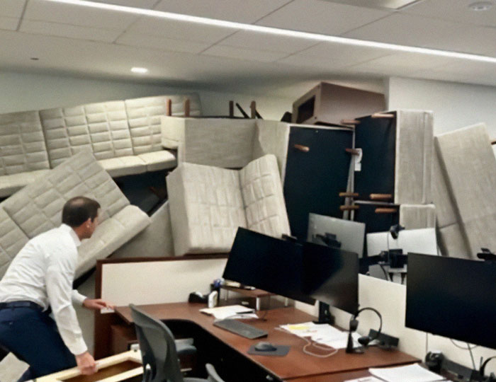 Office worker faces a large pile of overturned furniture blocking an office space.