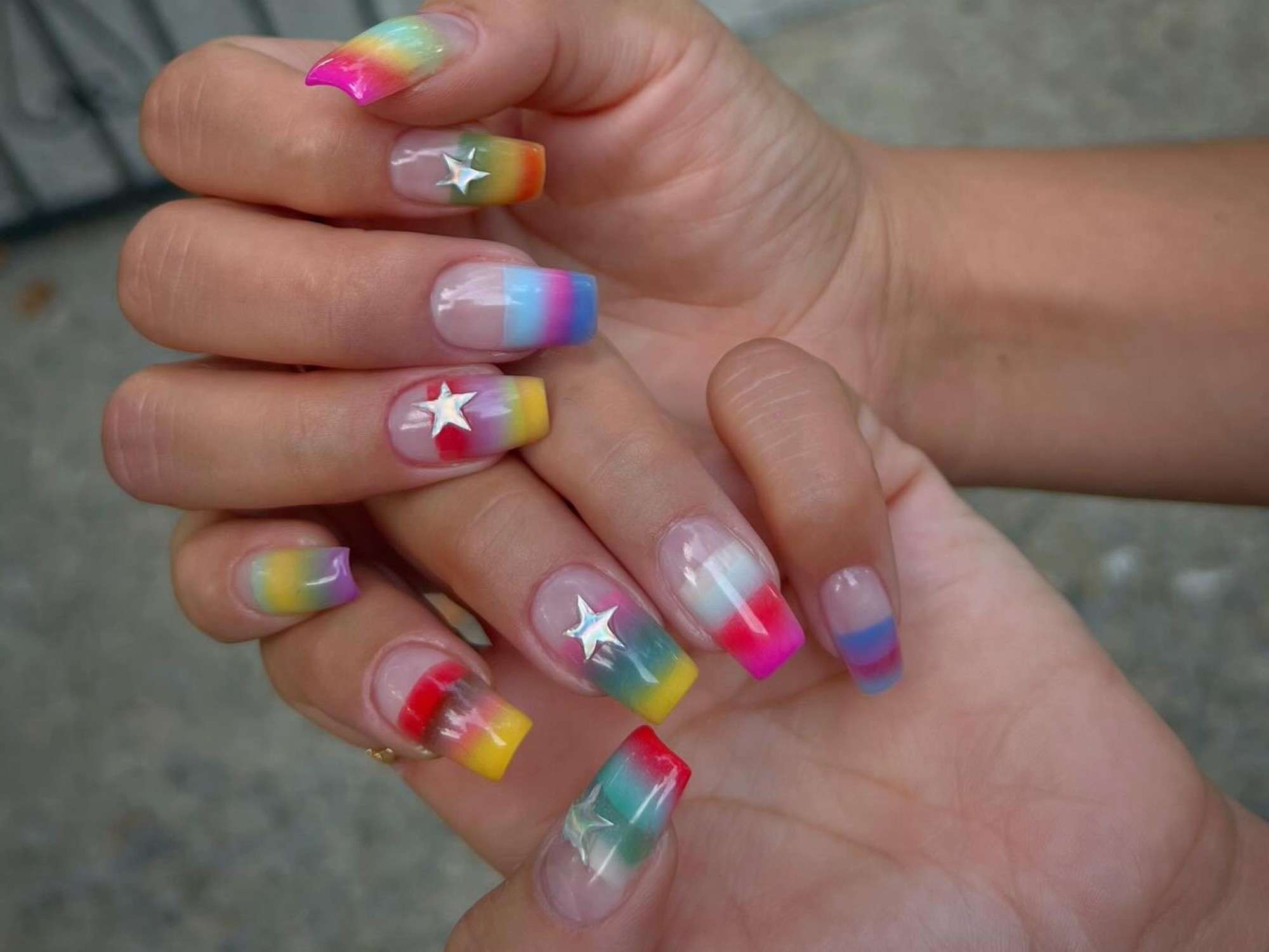 Colorful gradient nail art with silver star accents on a person's hands, showcasing a vibrant and creative manicure.