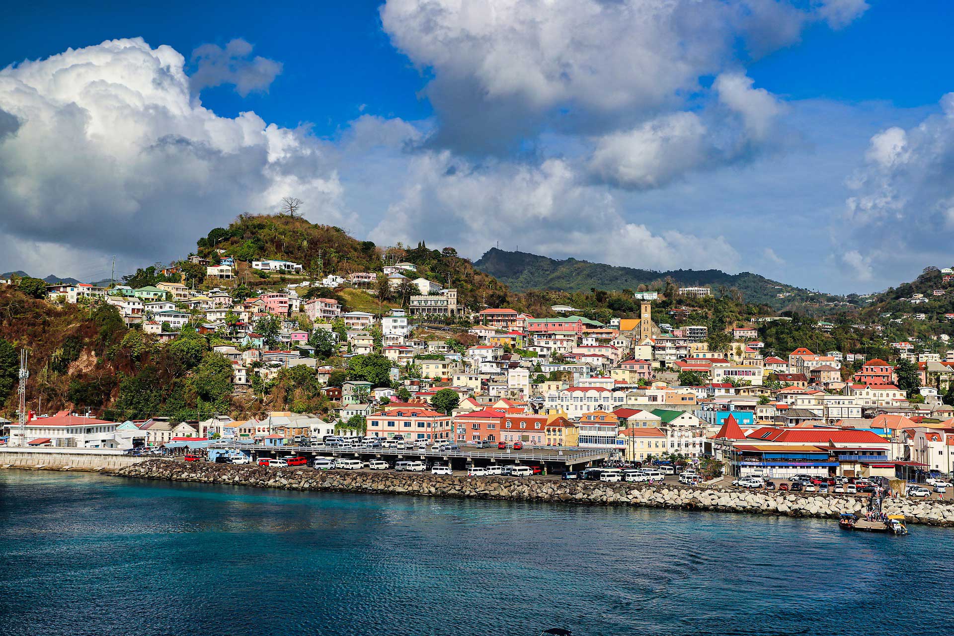 A city on the coast of Grenada with a harbor and mountains in the background