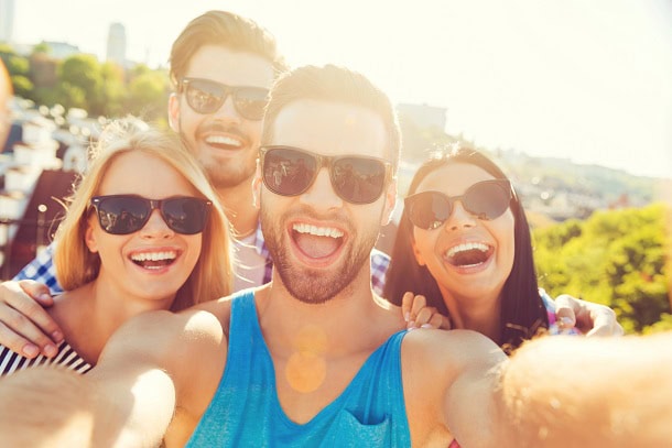 Four happy friends taking a selfie together in the summer sunshine.