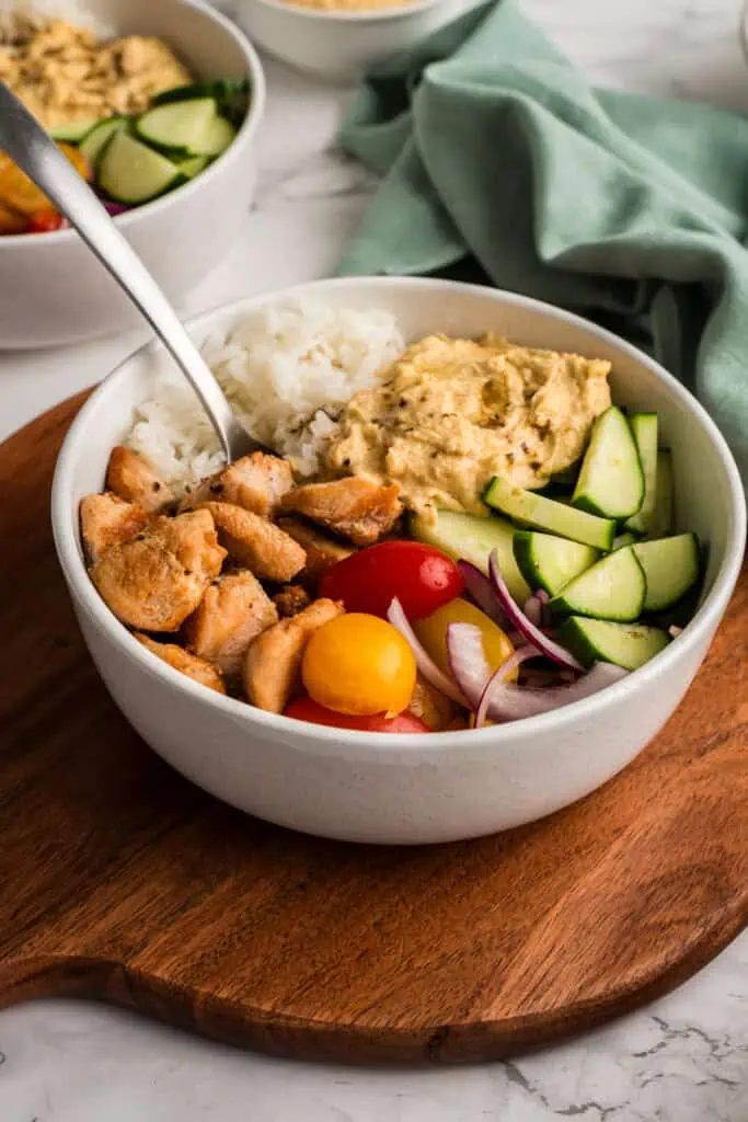 Greek Chicken and Rice Bowl on a wood cutting board with a fork resting in the bowl.