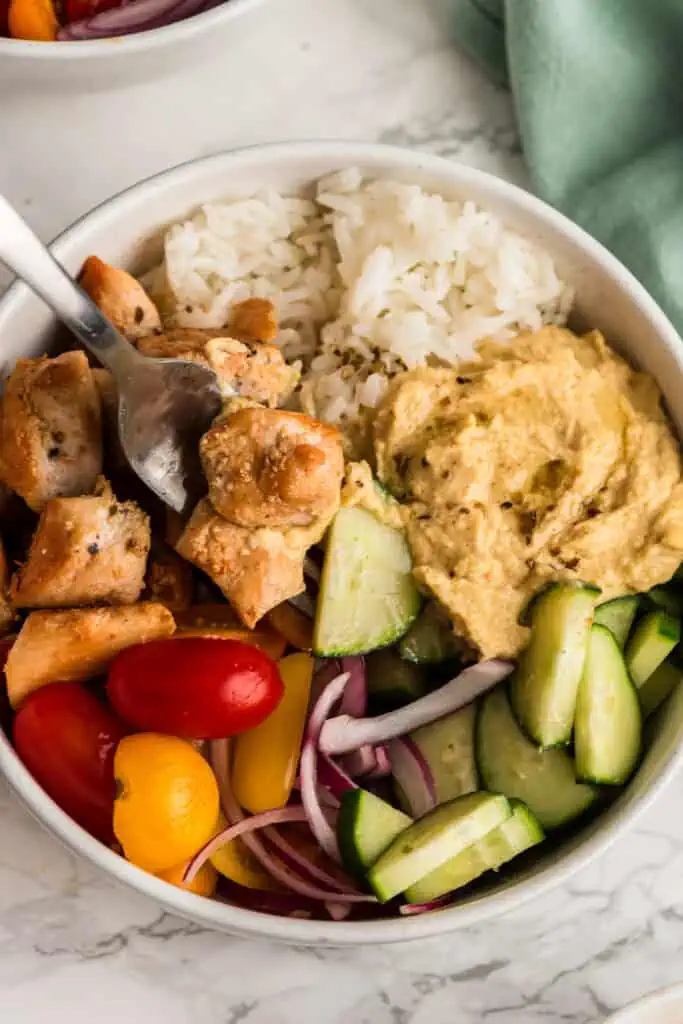 Fork resting in a bowl of Greek Chicken and Rice  on a marble countertop. 