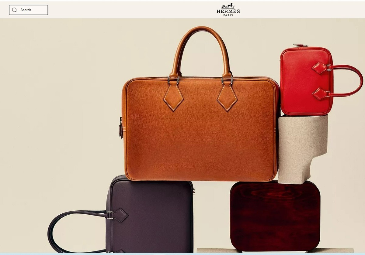 Elegant leather bags in various colors neatly stacked with Hermes Paris logo in the background.