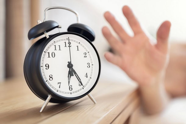 A hand reaching for the alarm clock beside the bed at 6.25 in the morning.