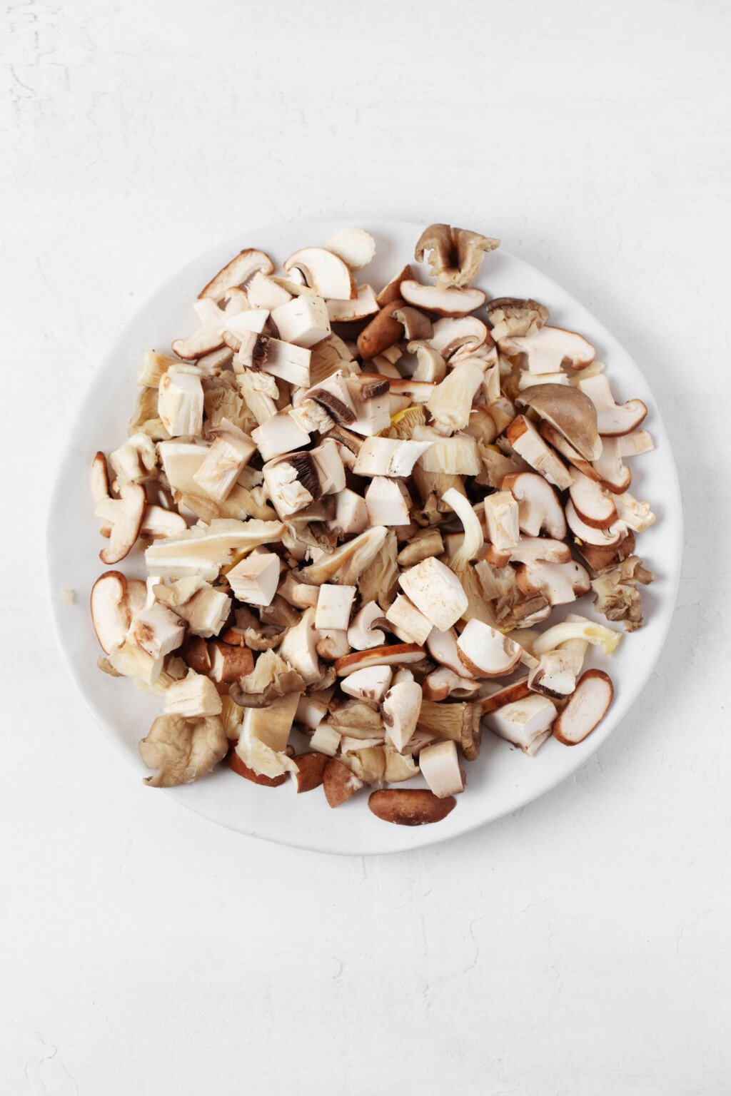 An overhead image of mixed, chopped mushrooms, arranged on a white plate.