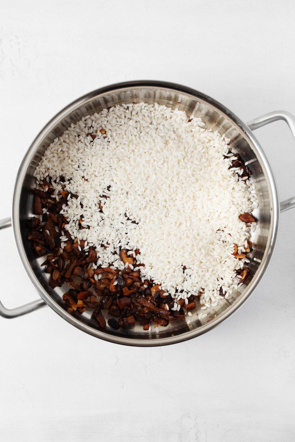 A large, heavy-bottomed pot is filled with rice and mushrooms. It's a dish of risotto in the making.