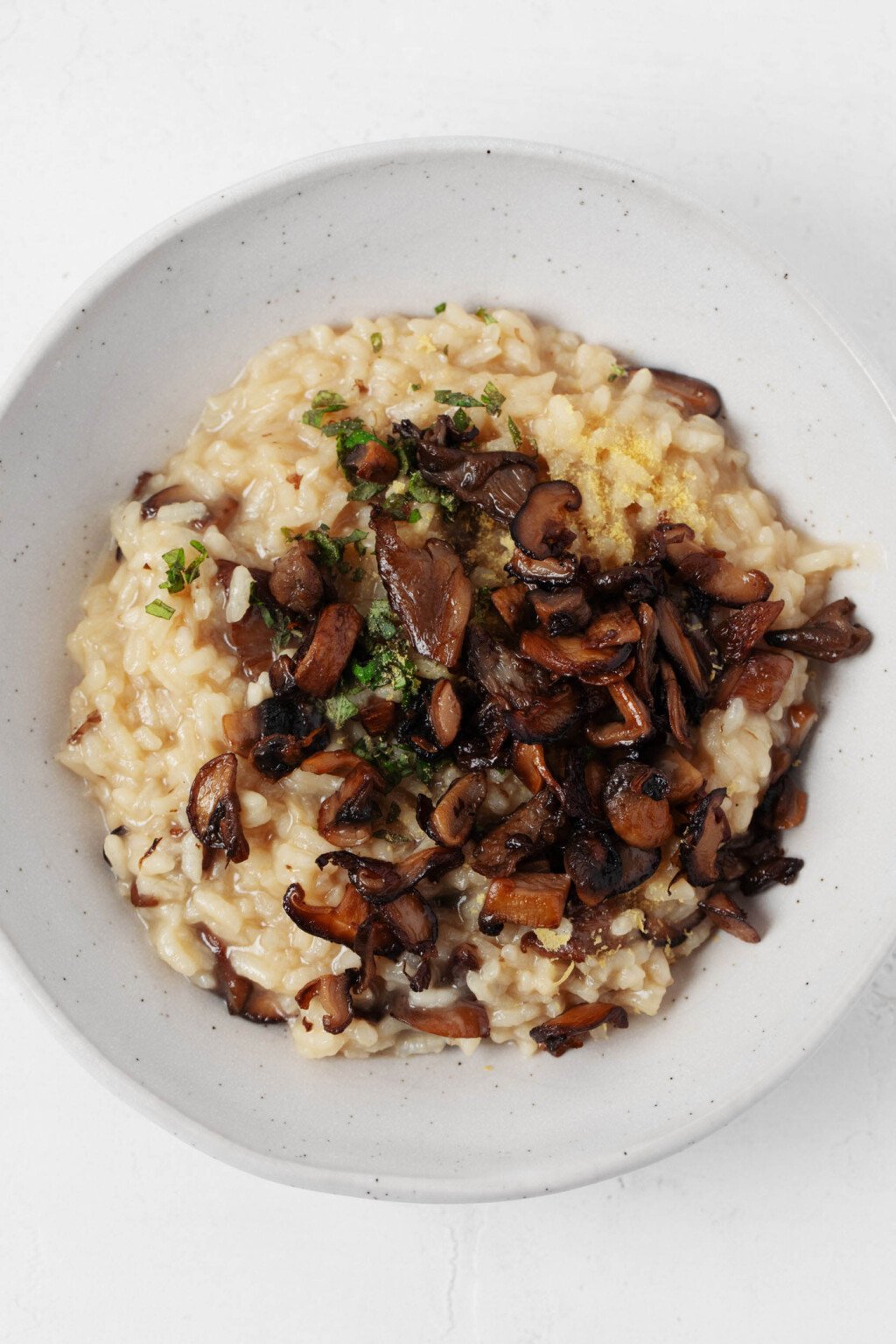 An overhead image of vegan mushroom risotto, which is garnished with green herbs and served in a white bowl. 