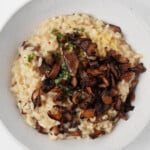 An overhead image of vegan mushroom risotto, which is garnished with green herbs and served in a white bowl.